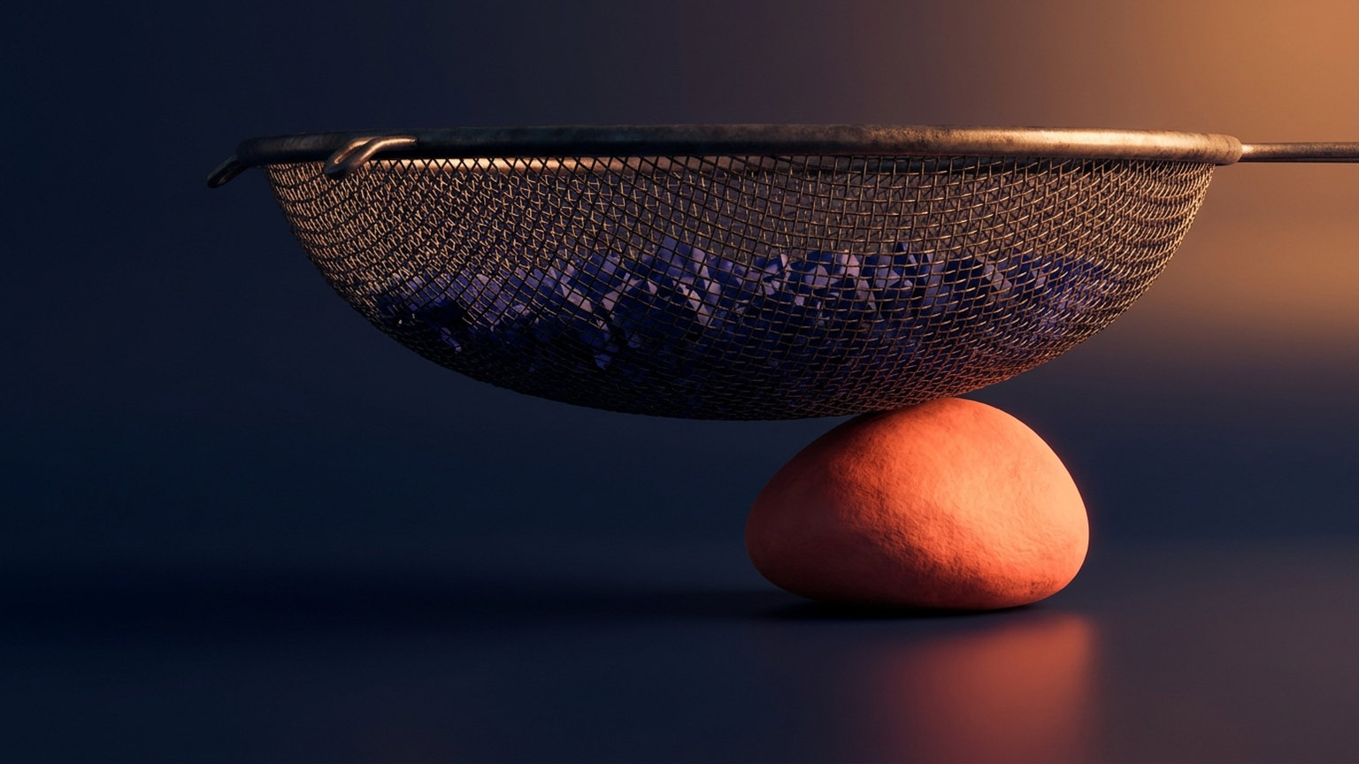 A fine wire mesh sieve holding a layer of small angular blue fragments, with one large smooth coral stone resting on the dark floor beneath it